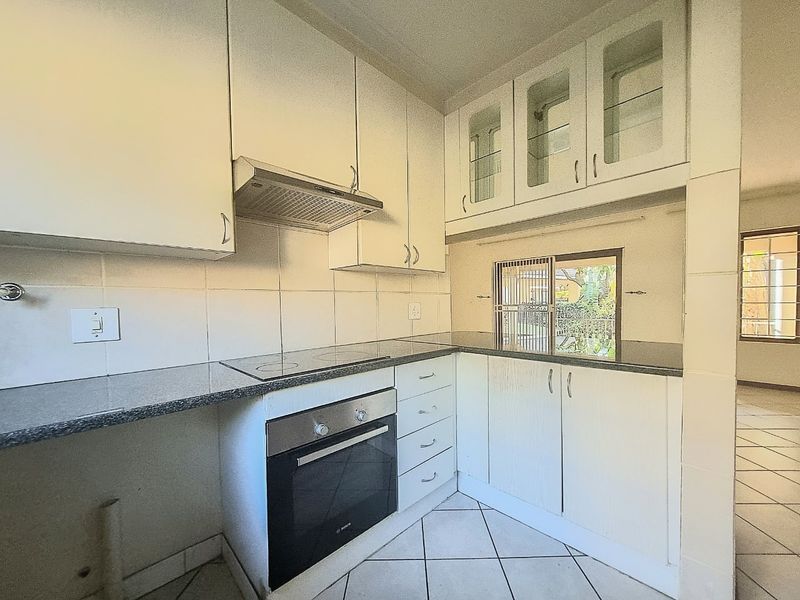 A functional kitchen featuring white built-in cabinetry, granite countertops, an integrated oven, and an electric hob, with tiled flooring throughout.