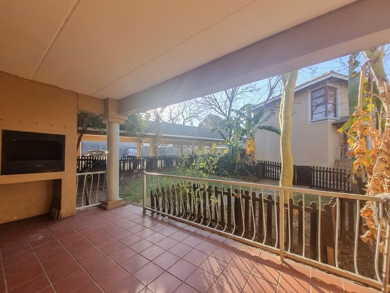 A covered patio featuring tiled flooring, a built-in braai, and a metal balustrade overlooking a private garden area.