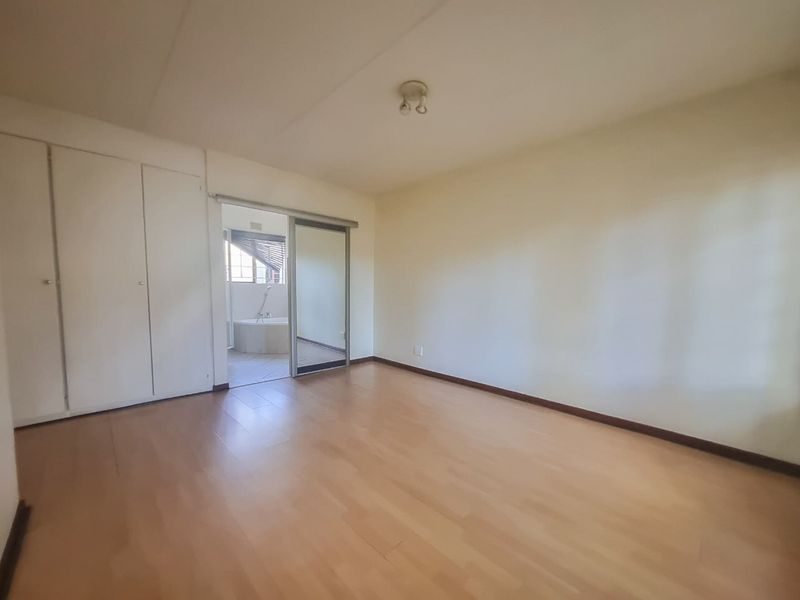 A spacious, empty bedroom featuring laminate flooring, built-in cupboards, and a sliding door leading to an en-suite bathroom area.