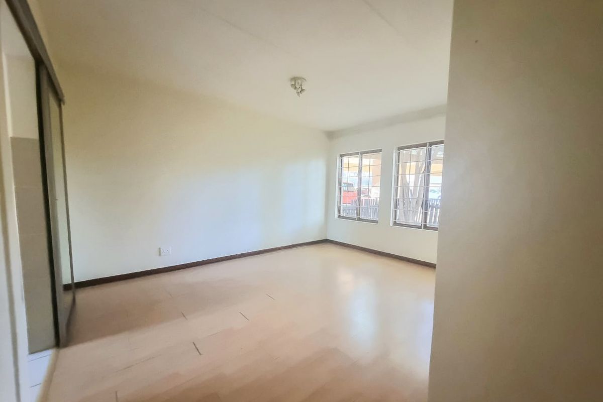 A spacious, empty bedroom featuring light-toned laminate flooring, a built-in sliding door wardrobe, and windows fitted with security burglar bars.