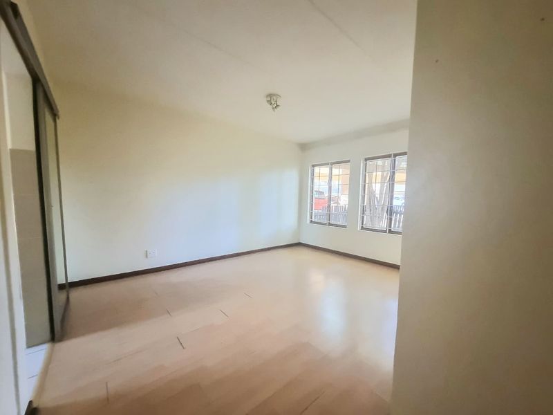 A spacious, empty bedroom featuring light-toned laminate flooring, a built-in sliding door wardrobe, and windows fitted with security burglar bars.