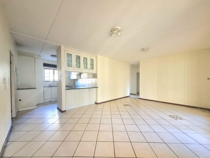 Spacious open-plan living area featuring tiled flooring and a functional kitchen with built-in cabinetry and glass-fronted display units.