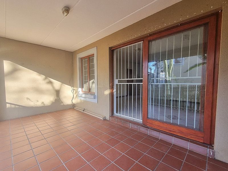 A covered patio area featuring terracotta-style floor tiles, a sliding glass door with security gate, and a window with security bars.