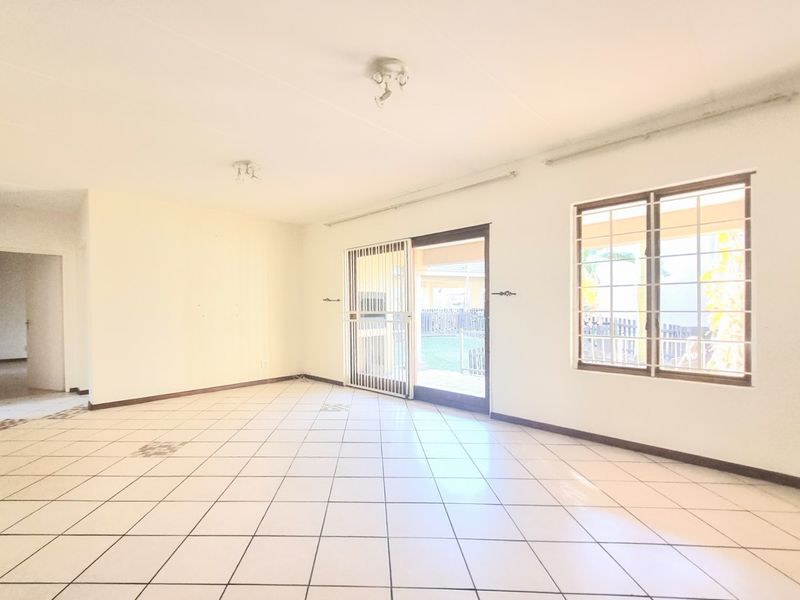 An empty, open-plan living area featuring tiled flooring, large windows with security bars, and a sliding door providing access to the rear exterior.