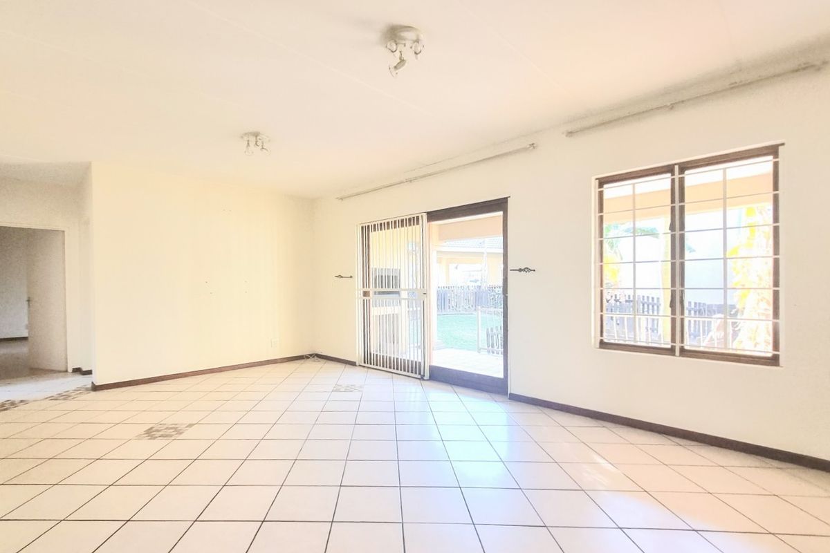 An empty, open-plan living area featuring tiled flooring, large windows with security bars, and a sliding door providing access to the rear exterior.