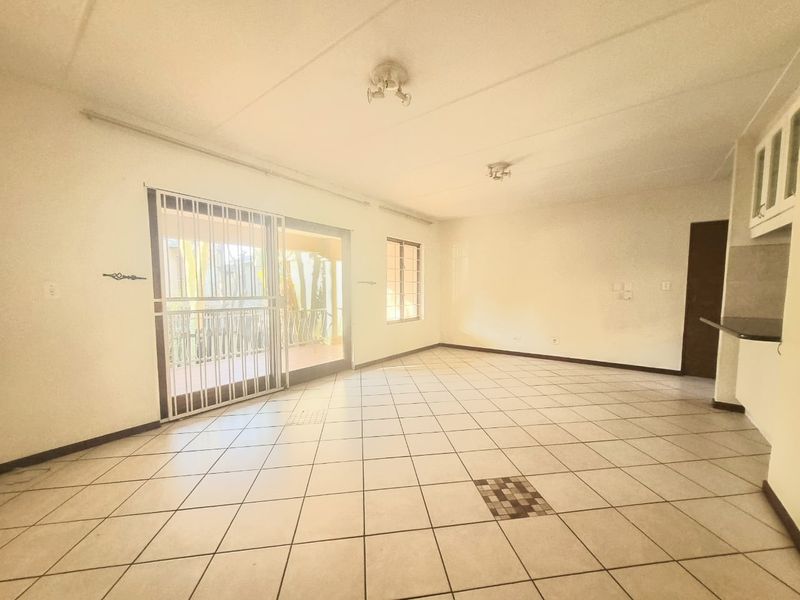 Spacious open-plan living area featuring tiled flooring, a sliding door with security gate, and direct access to an outdoor patio space.