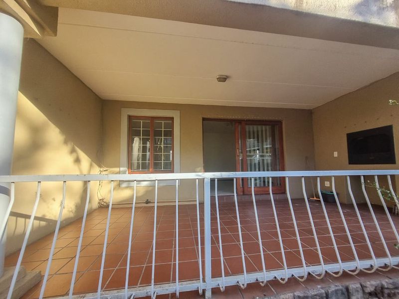 A covered patio area featuring tiled flooring, a built-in braai, and a metal security railing, providing a functional outdoor space for relaxation.