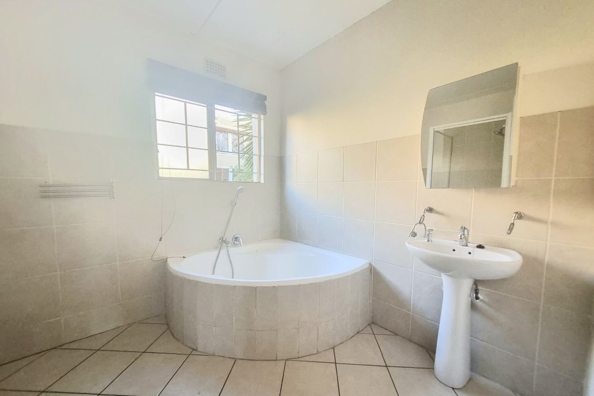 A functional bathroom featuring a corner bathtub, pedestal basin, and neutral wall and floor tiling, offering a blank canvas for modern updates.