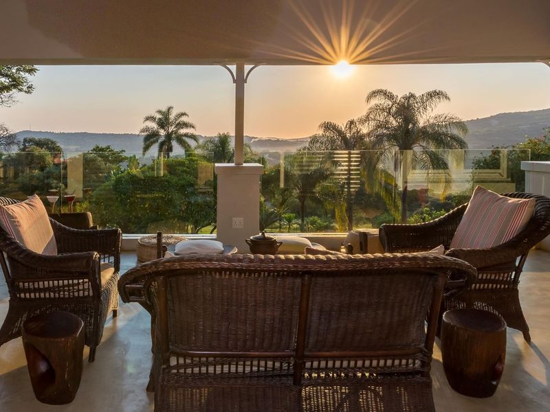 A spacious covered patio featuring a modern glass balustrade and scenic sunset views over the surrounding landscape.