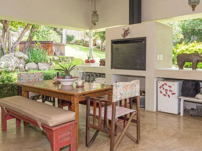 A spacious covered patio featuring a built-in braai and concrete flooring, overlooking a lush garden setting, ideal for outdoor dining and entertainment.