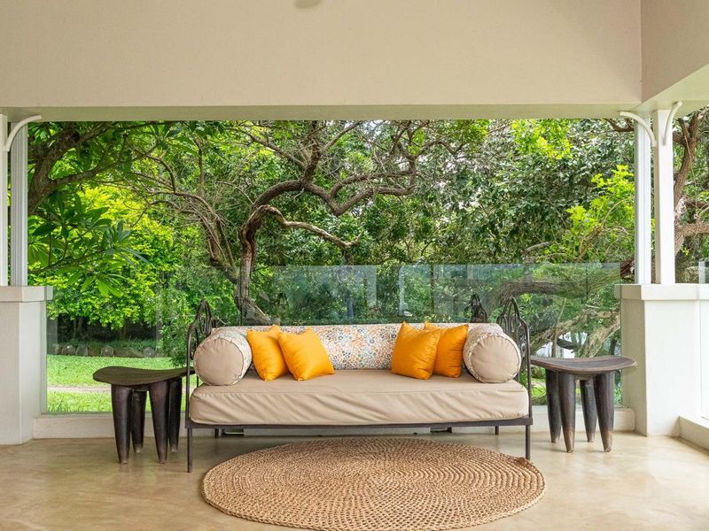 A covered patio area featuring a sleek glass balustrade and polished concrete flooring, offering a serene view of the surrounding lush garden.