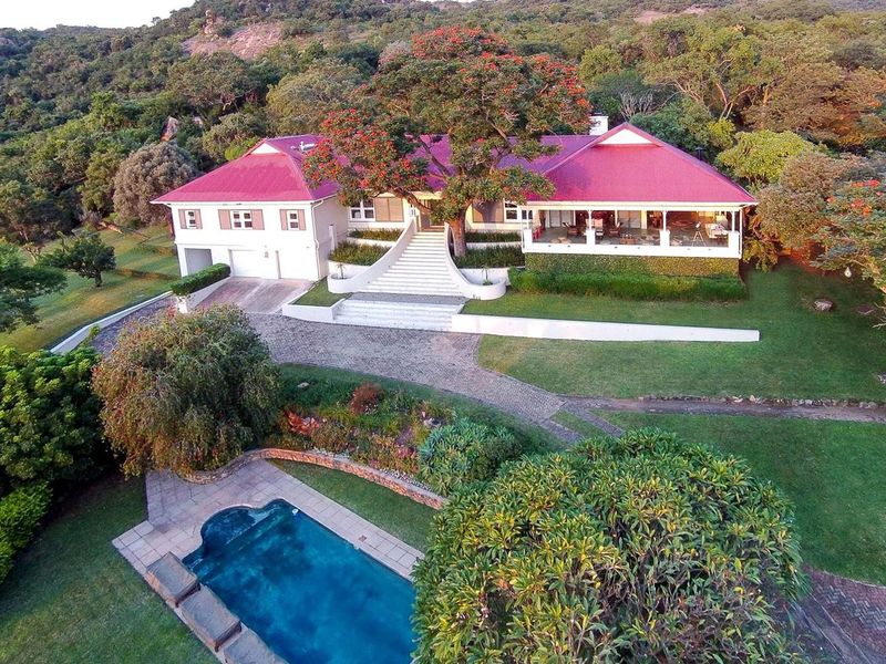 Aerial view of a large farm property featuring a main residence with a red metal roof, swimming pool, and extensive landscaped grounds.