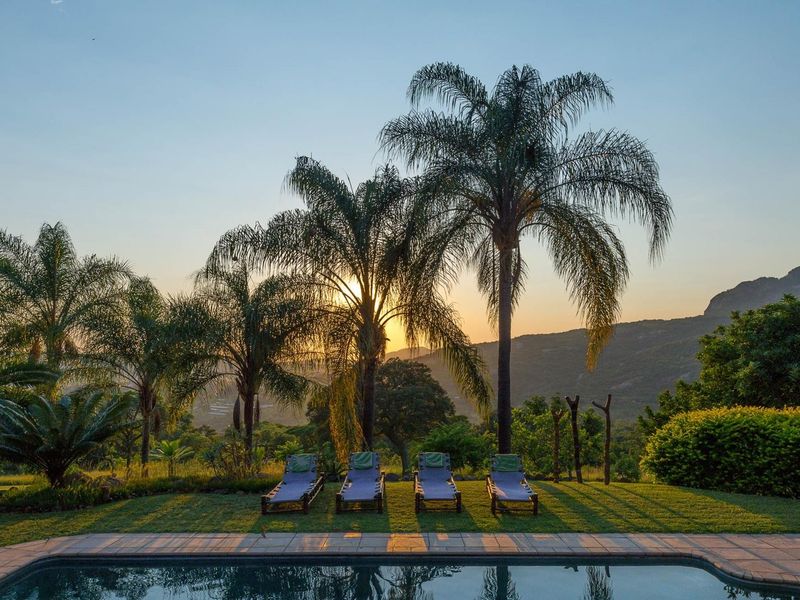 A serene outdoor pool area featuring stone coping, lush garden surroundings, and scenic mountain views at sunset.