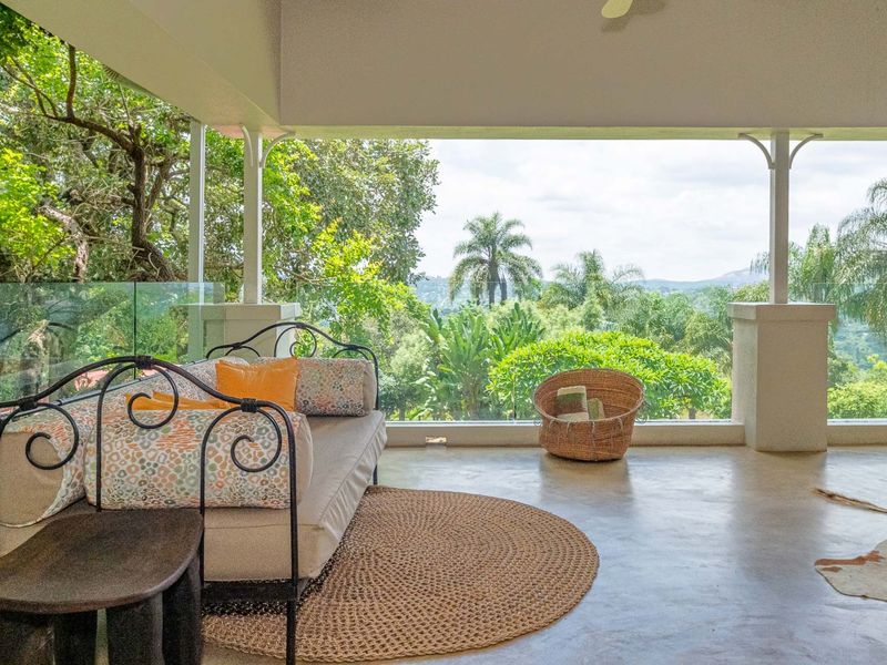 A covered patio featuring polished concrete floors, a glass balustrade, and expansive views of the surrounding lush landscape.