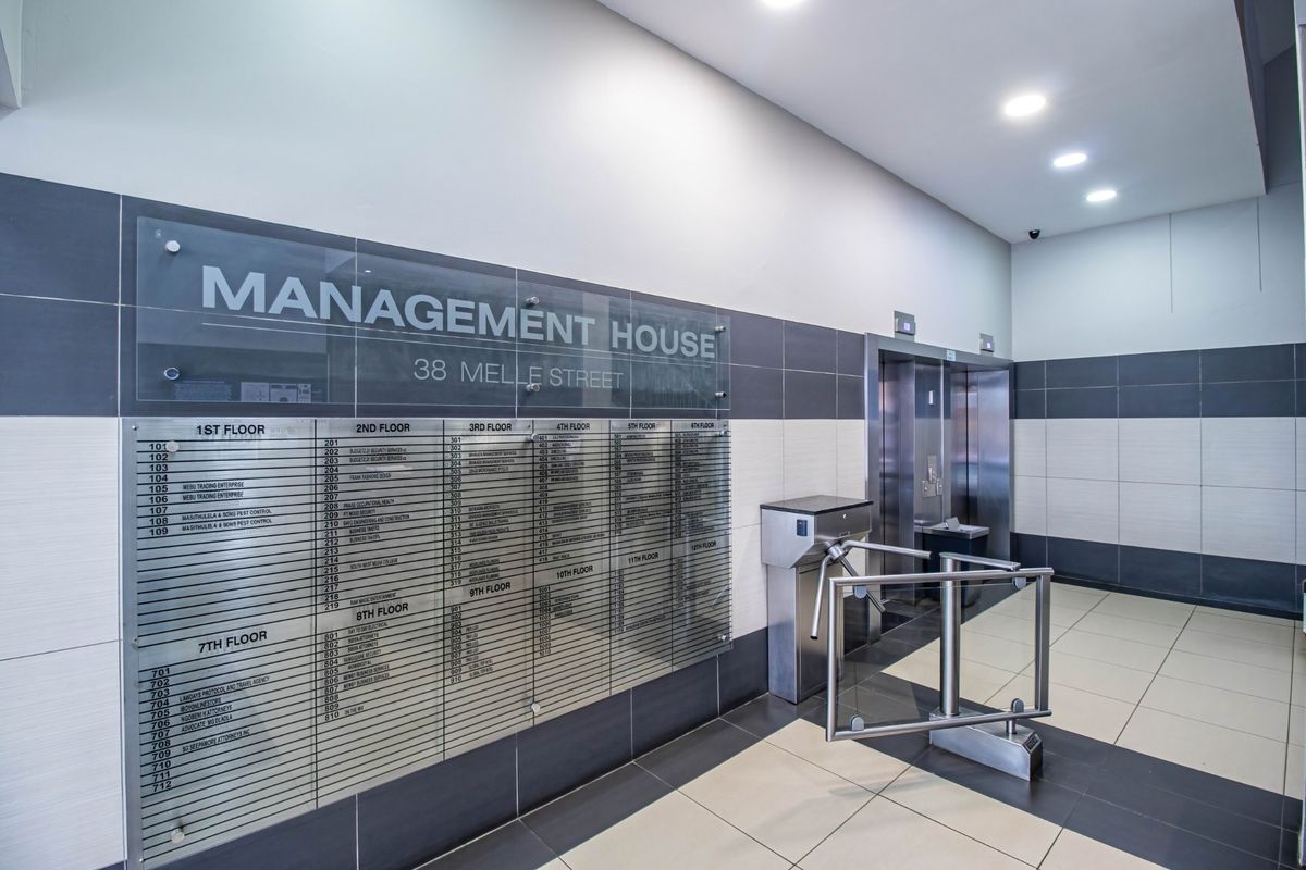 Modern commercial building lobby featuring a clear tenant directory board, secure turnstile access, and elevator bank with contemporary tiled finishes.