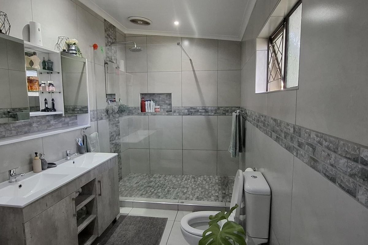 Modern bathroom featuring a double vanity, spacious walk-in shower with a rain shower head, recessed niche, and contemporary tiled finishes.