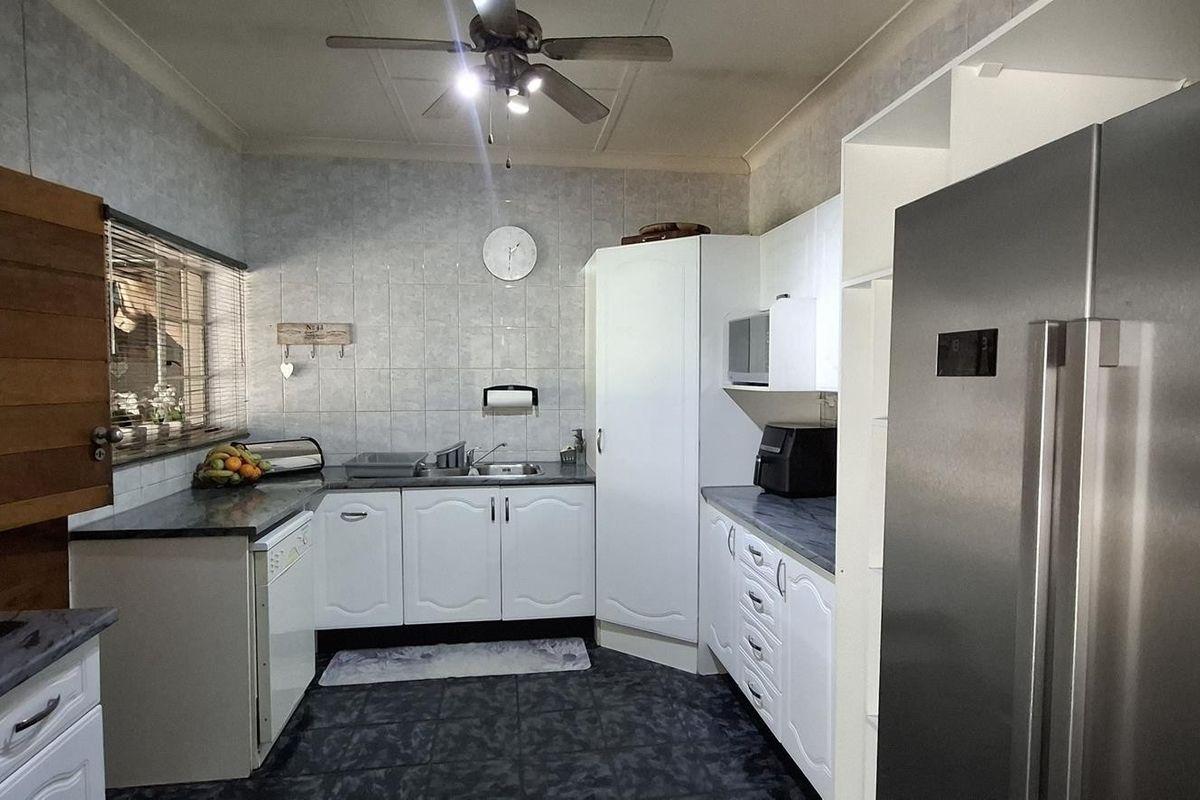 A functional kitchen featuring white cabinetry, dark tiled flooring, tiled splashbacks, and a ceiling fan, providing a practical workspace with ample storage.