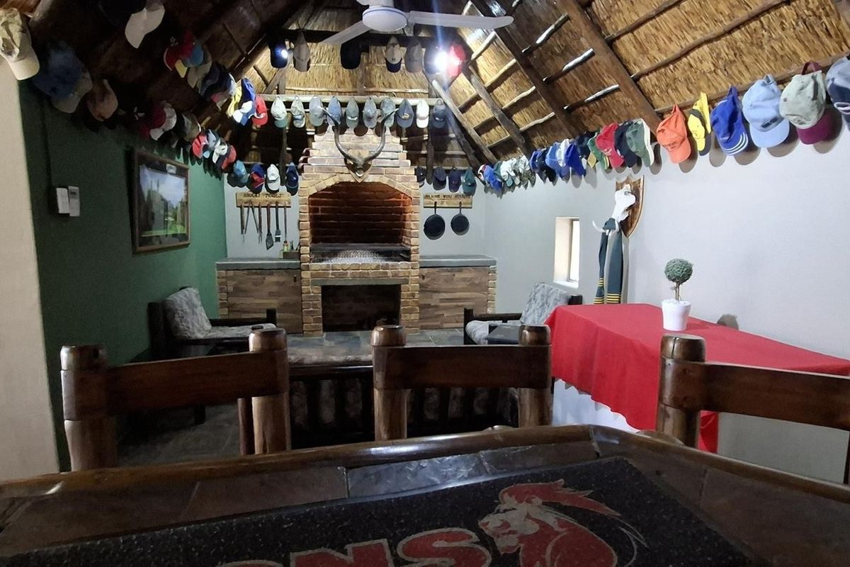 Rustic living area featuring a traditional thatched roof with exposed timber rafters and a prominent built-in brick fireplace.