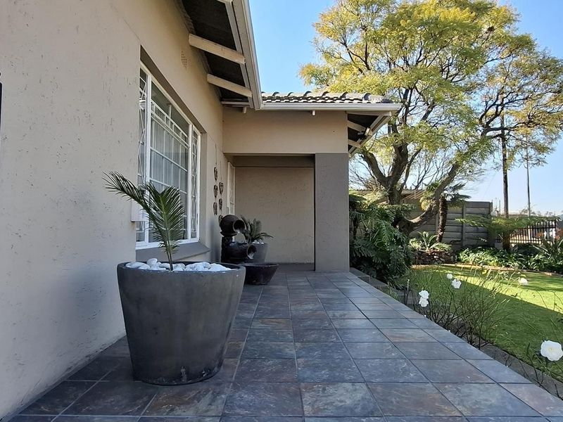 A well-maintained covered patio area featuring durable tiled flooring, overlooking a landscaped garden with a wrought iron entrance gate.