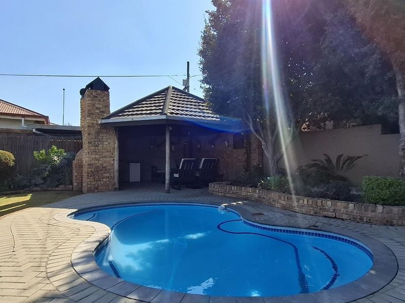 Outdoor entertainment area featuring a swimming pool, paved surround, and a brick-built braai structure under a thatched lapa.