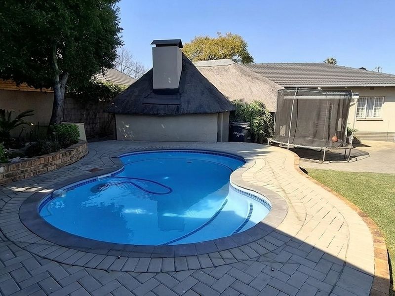 Outdoor entertainment area featuring a swimming pool, paved surround, and a traditional thatched lapa structure in the rear garden.