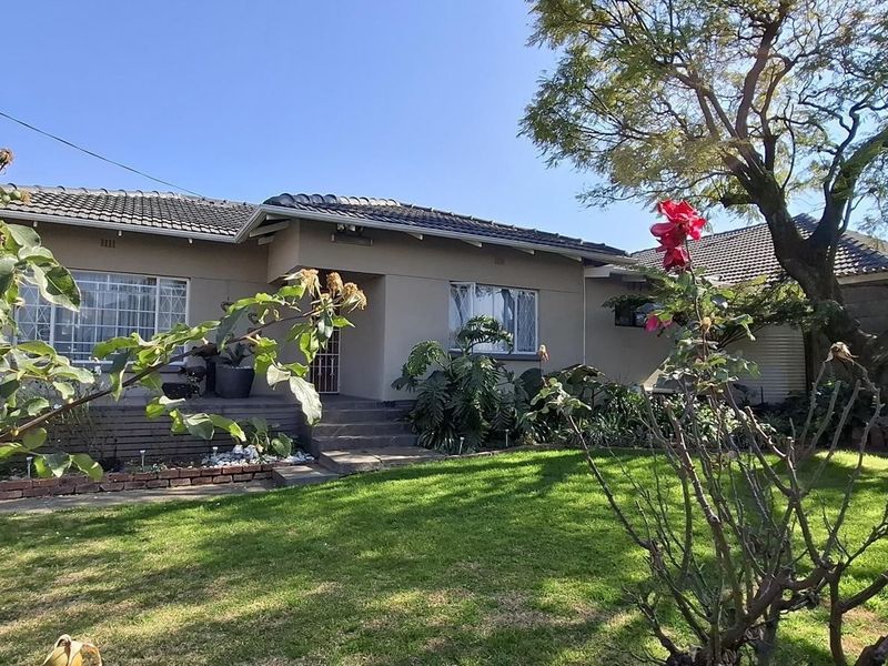 Front view of a single-story residential house featuring a tiled roof, concrete entrance steps, and a well-maintained front garden with mature trees.