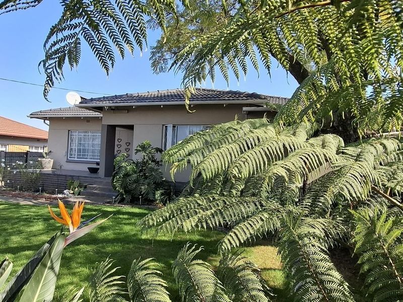 Front view of a single-story residential house featuring a tiled roof, security bars on windows, and a well-maintained front garden with mature ferns.