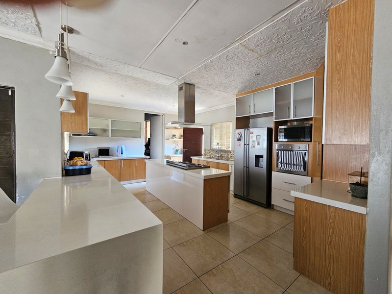 Spacious kitchen featuring a central island with gas hob, stone countertops, built-in appliances, and ample wooden cabinetry with tiled flooring throughout.