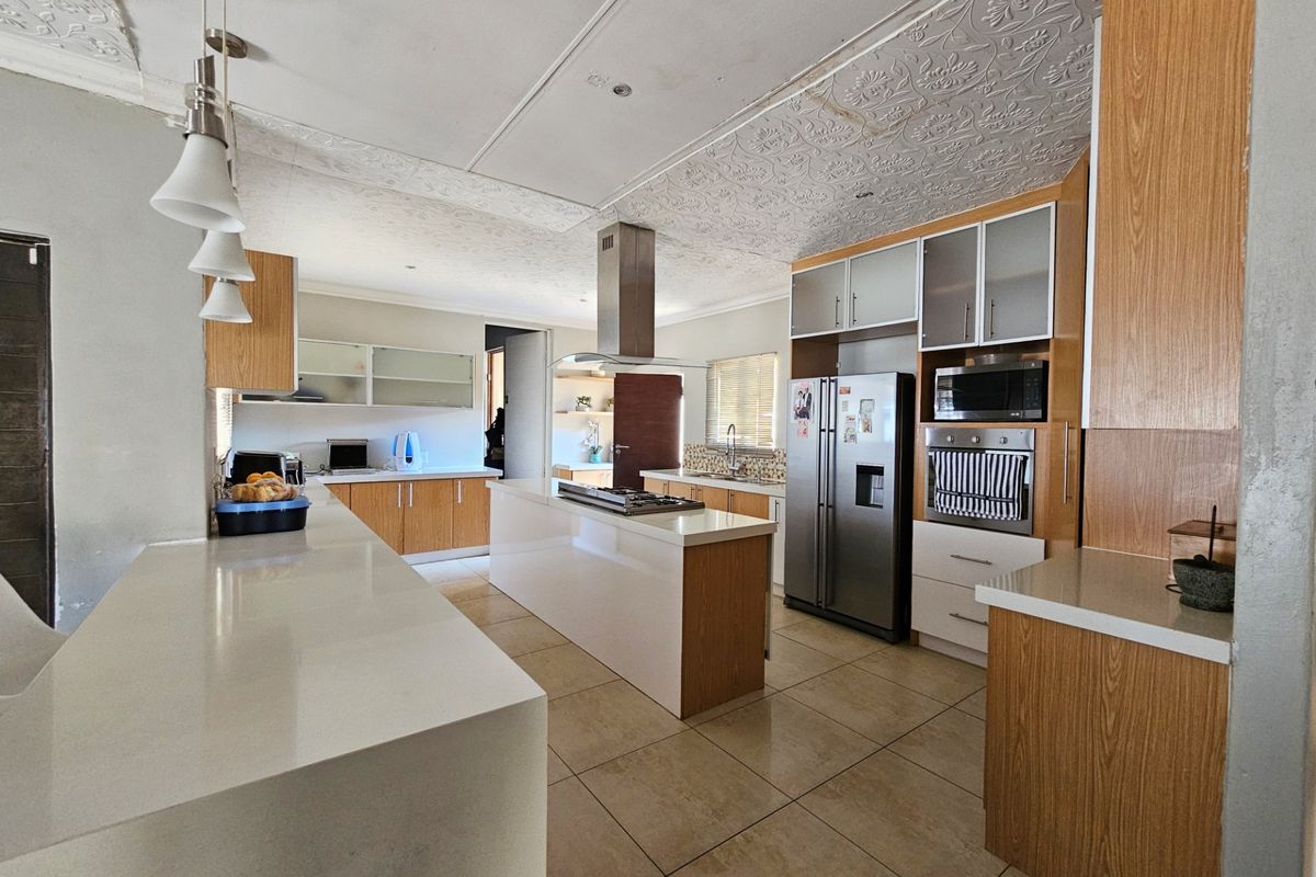 Spacious kitchen featuring a central island with gas hob, stone countertops, built-in appliances, and ample wooden cabinetry with tiled flooring throughout.