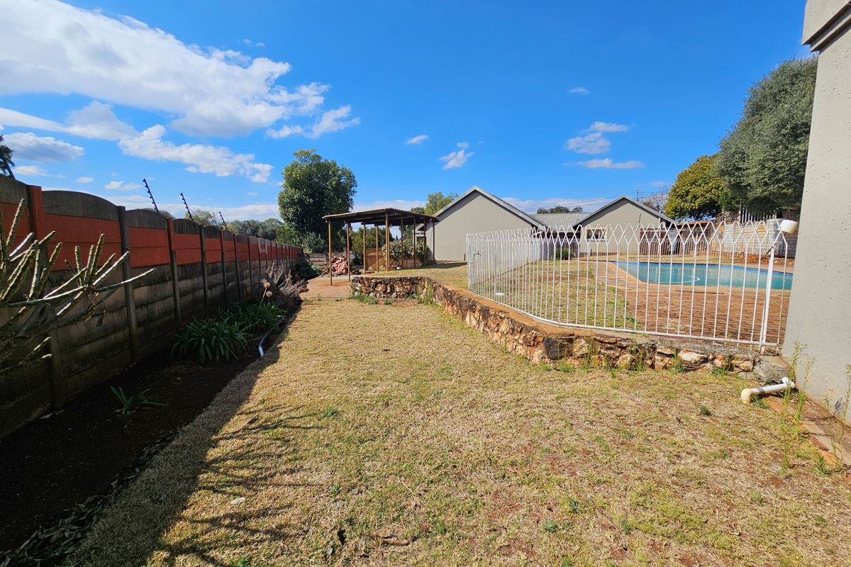 Spacious rear garden featuring a swimming pool with safety fencing, a stone retaining wall, a pergola, and a precast concrete boundary wall.