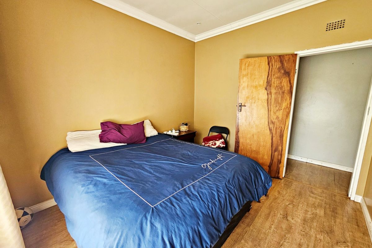 A standard bedroom featuring laminate flooring, crown molding, and a wooden door, providing a functional space ready for cosmetic updates.