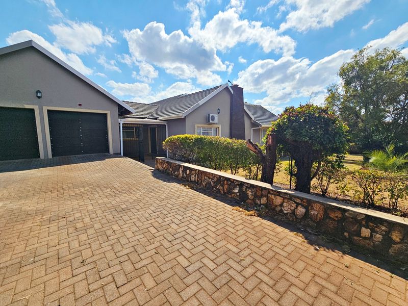 Front exterior view of the house featuring a paved driveway, double garage, and a stone retaining wall with established garden landscaping.