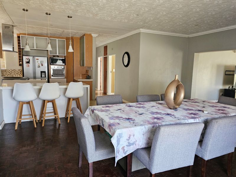 Open-plan living and dining area featuring a functional kitchen with built-in cabinetry, island seating, and parquet flooring throughout.