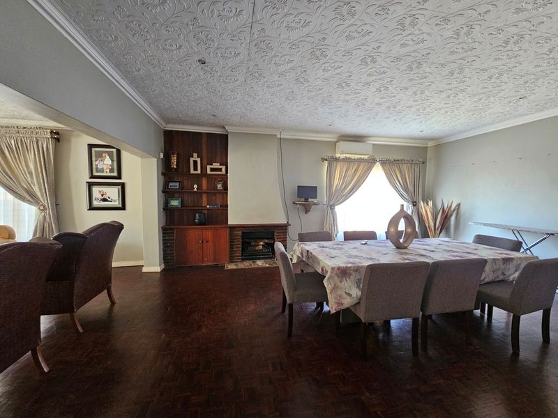 Spacious open-plan living and dining area featuring classic parquet flooring, a built-in fireplace with wooden shelving, and a decorative textured ceiling.