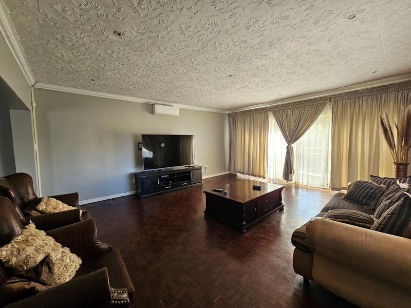 Spacious living room featuring dark parquet flooring, a decorative textured ceiling, and a wall-mounted air conditioning unit with access to an outdoor area.