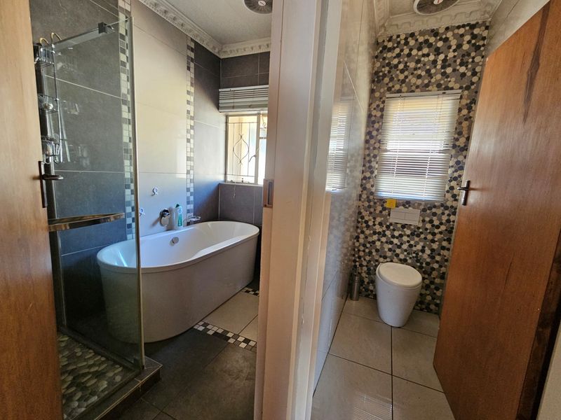 A modern bathroom featuring a freestanding bathtub, a separate glass-enclosed shower, and a wall-hung toilet with decorative mosaic wall tiling.