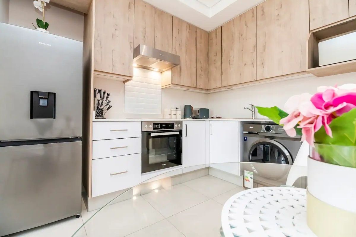 Modern kitchen featuring light wood-tone cabinetry, white countertops, subway tile backsplash, integrated oven, and sleek tiled flooring.