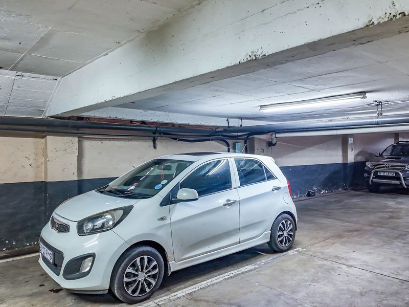 Underground commercial parking garage featuring exposed concrete beams, industrial piping, and fluorescent lighting.