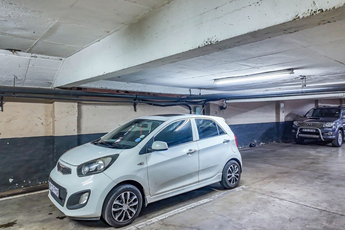 Underground commercial parking garage featuring exposed concrete beams, industrial piping, and fluorescent lighting.