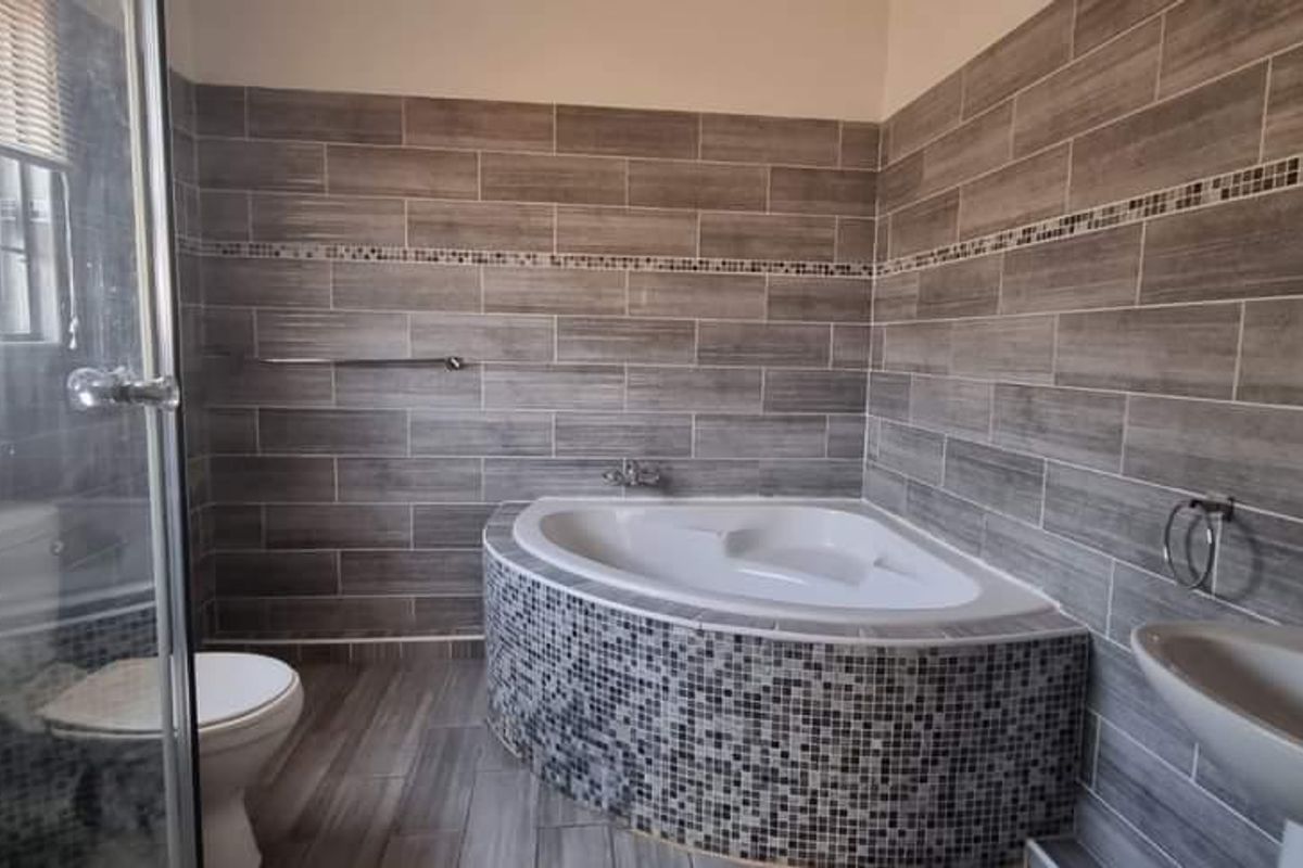 A modern bathroom featuring a corner bathtub with mosaic tiling, a separate glass shower enclosure, a pedestal basin, and neutral grey wall tiles.