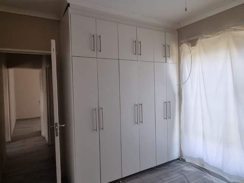 A bright, empty bedroom featuring modern white built-in cupboards, laminate flooring, and neutral wall tones, offering a clean and versatile living space.