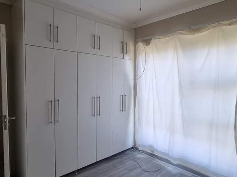 A bright, empty bedroom featuring modern white built-in cupboards, tiled flooring, and neutral wall finishes, offering a clean canvas for personalization.