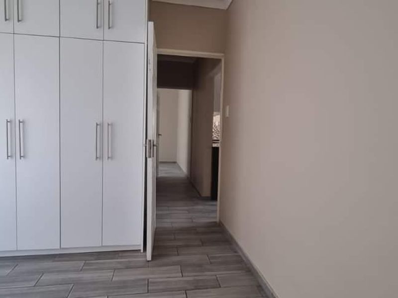 A clean, empty bedroom featuring modern white built-in cupboards and neutral tiled flooring, leading into a hallway.