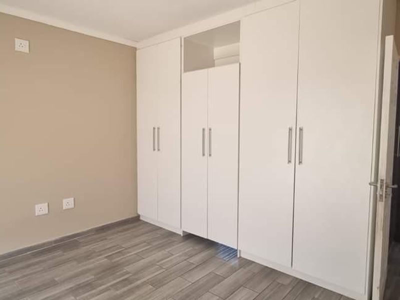 A clean, empty bedroom featuring modern grey tiled flooring and extensive white built-in cupboards, offering a neutral canvas for personalization.