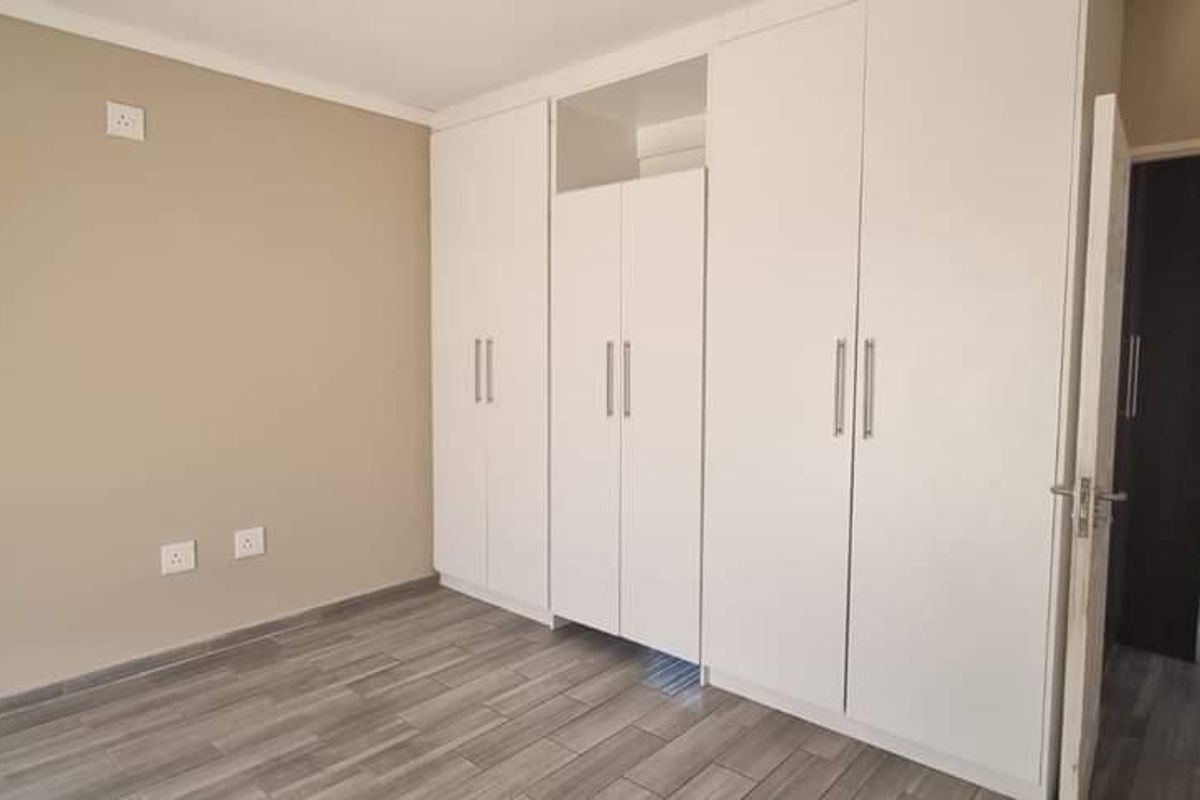 A clean, empty bedroom featuring modern grey tiled flooring and extensive white built-in cupboards, offering a neutral canvas for personalization.