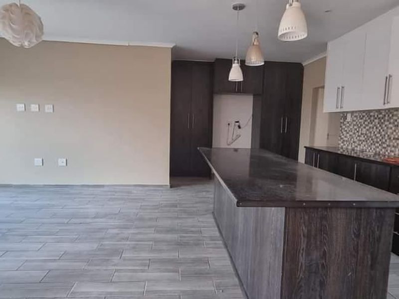 Spacious open-plan living and kitchen area featuring a large island, modern cabinetry, mosaic backsplash, and tiled flooring throughout.