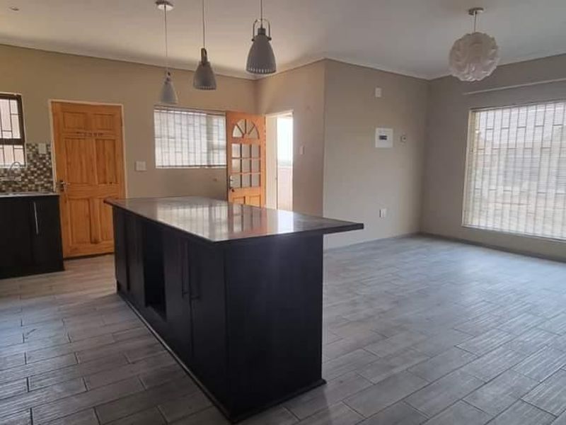 Spacious open-plan living area featuring a modern kitchen with a central island, dark cabinetry, gas hob, and neutral tiled flooring throughout.
