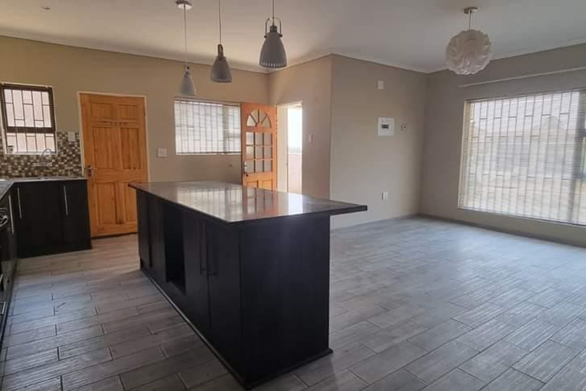 Spacious open-plan living area featuring a modern kitchen with a central island, dark cabinetry, gas hob, and neutral tiled flooring throughout.