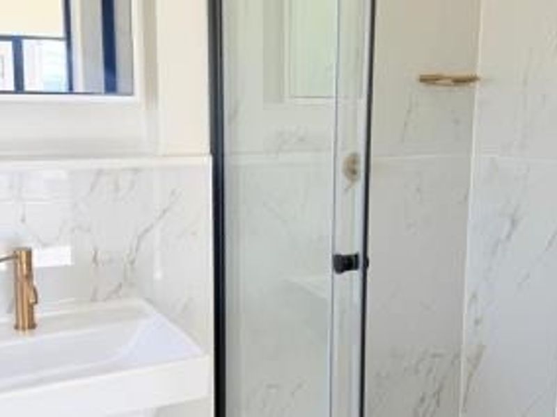 Modern bathroom featuring marble-look wall tiles, a glass shower enclosure, and a contemporary brass faucet with a wall-mounted basin.