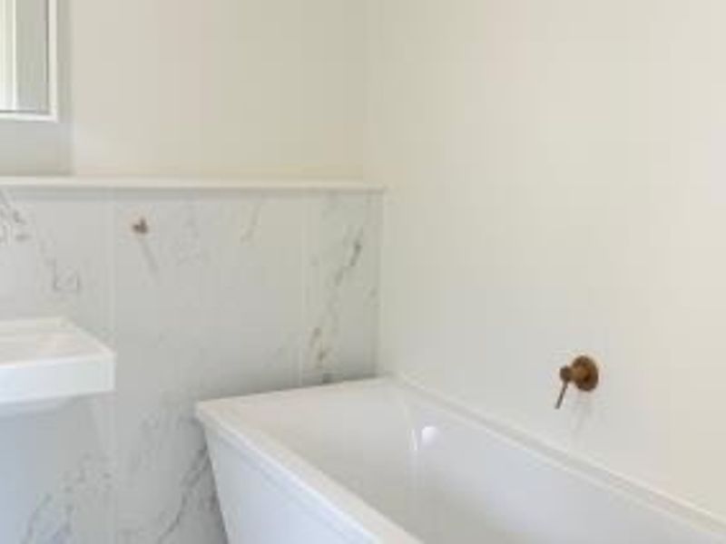 Modern bathroom featuring a clean white freestanding bathtub, marble-look wall tiling, and elegant brass-finish wall-mounted tapware.